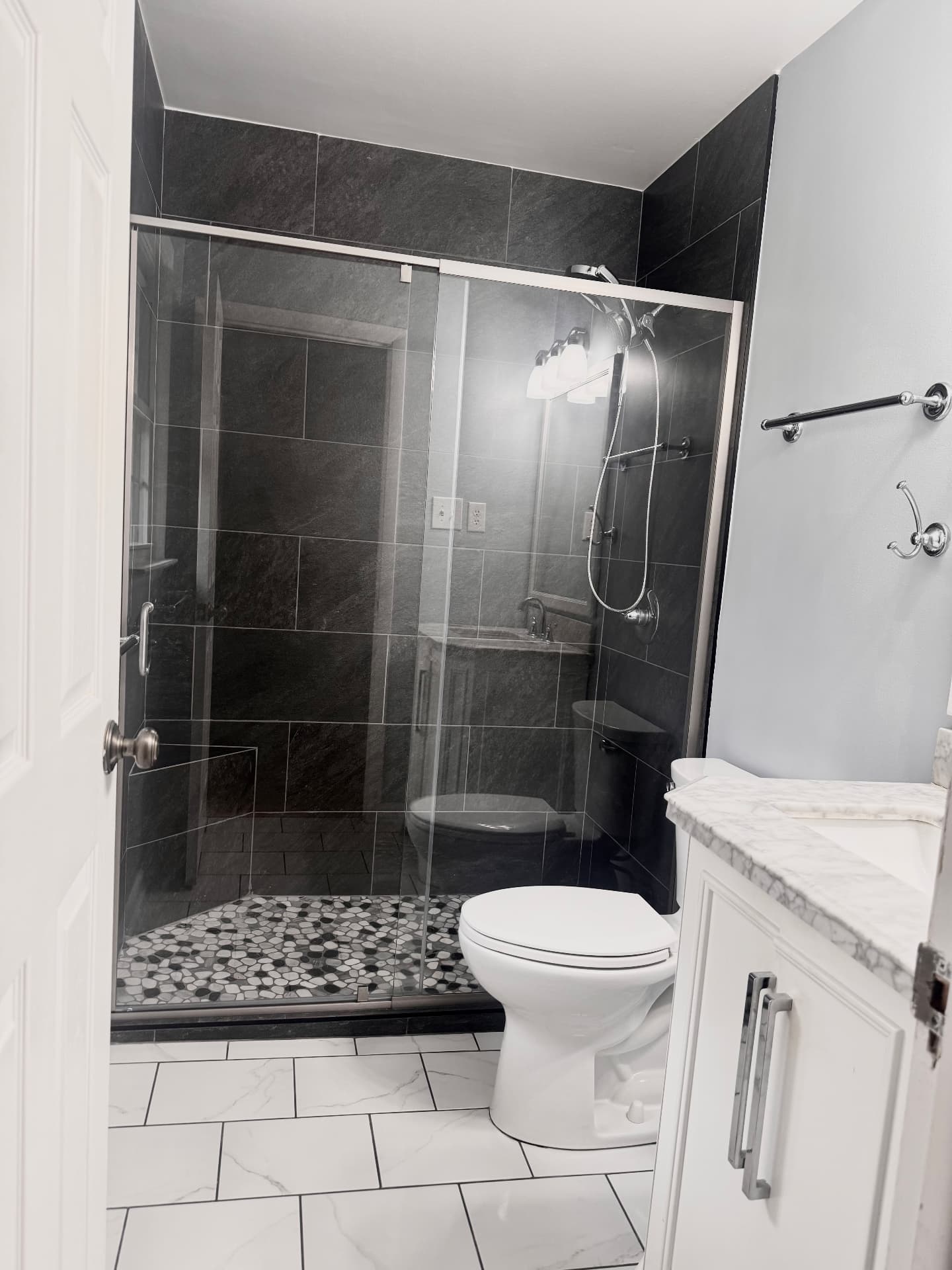 Bathroom remodel with dark slate tile shower, pebble mosaic floor, and marble-top white vanity