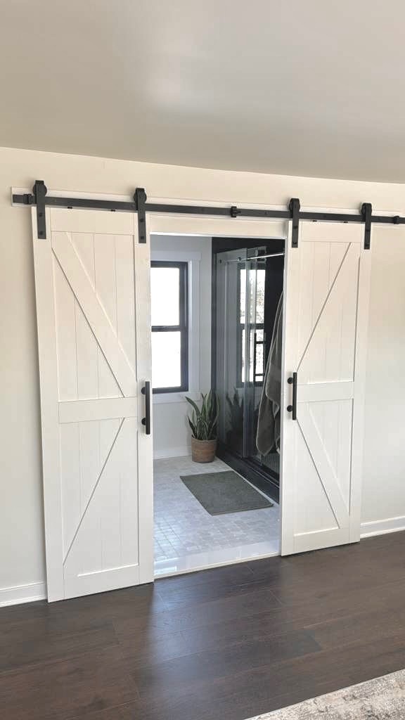 White double barn doors on black hardware leading into a remodeled bathroom